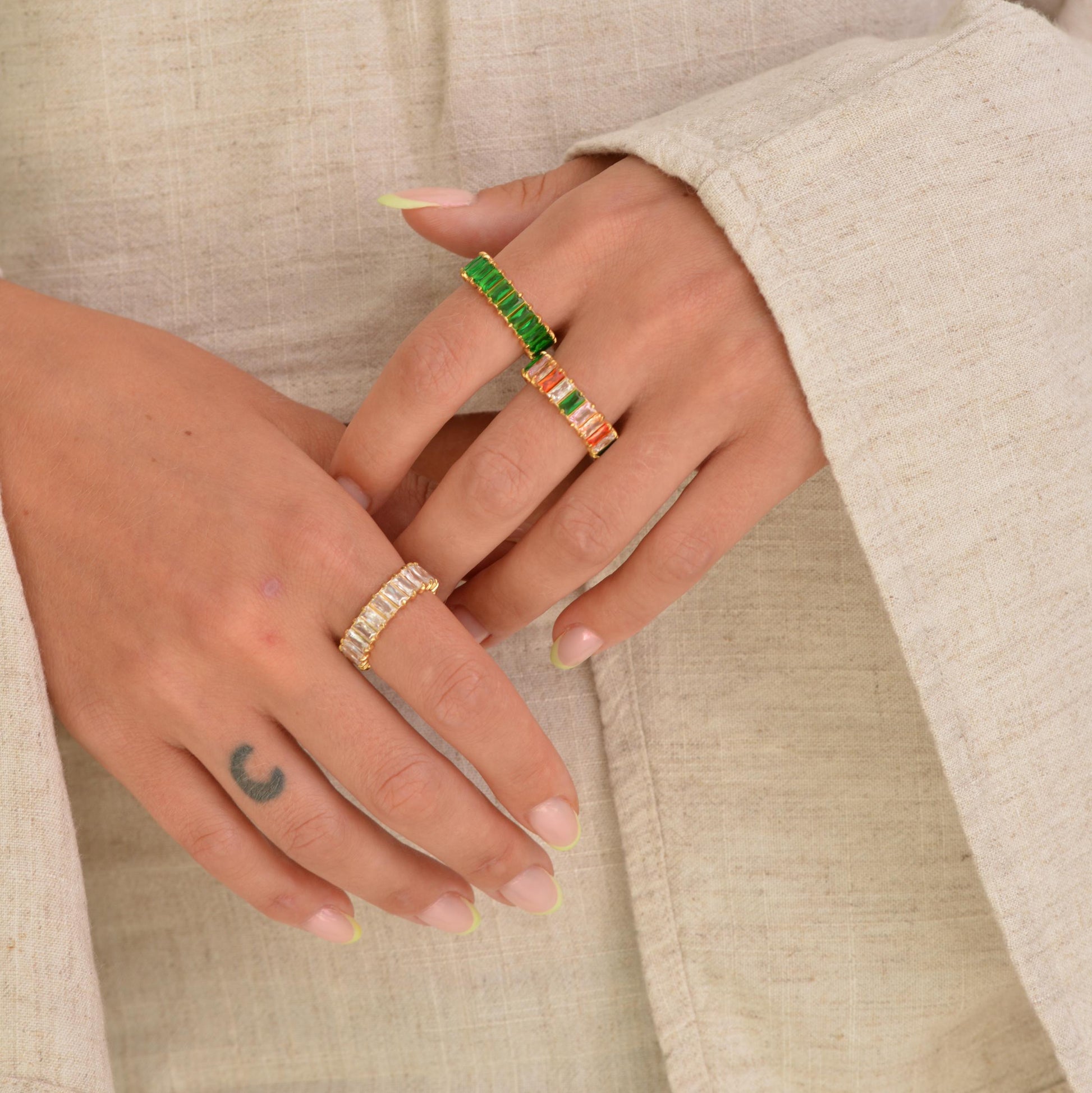 Close-up of hands wearing multiple rings on a neutral background