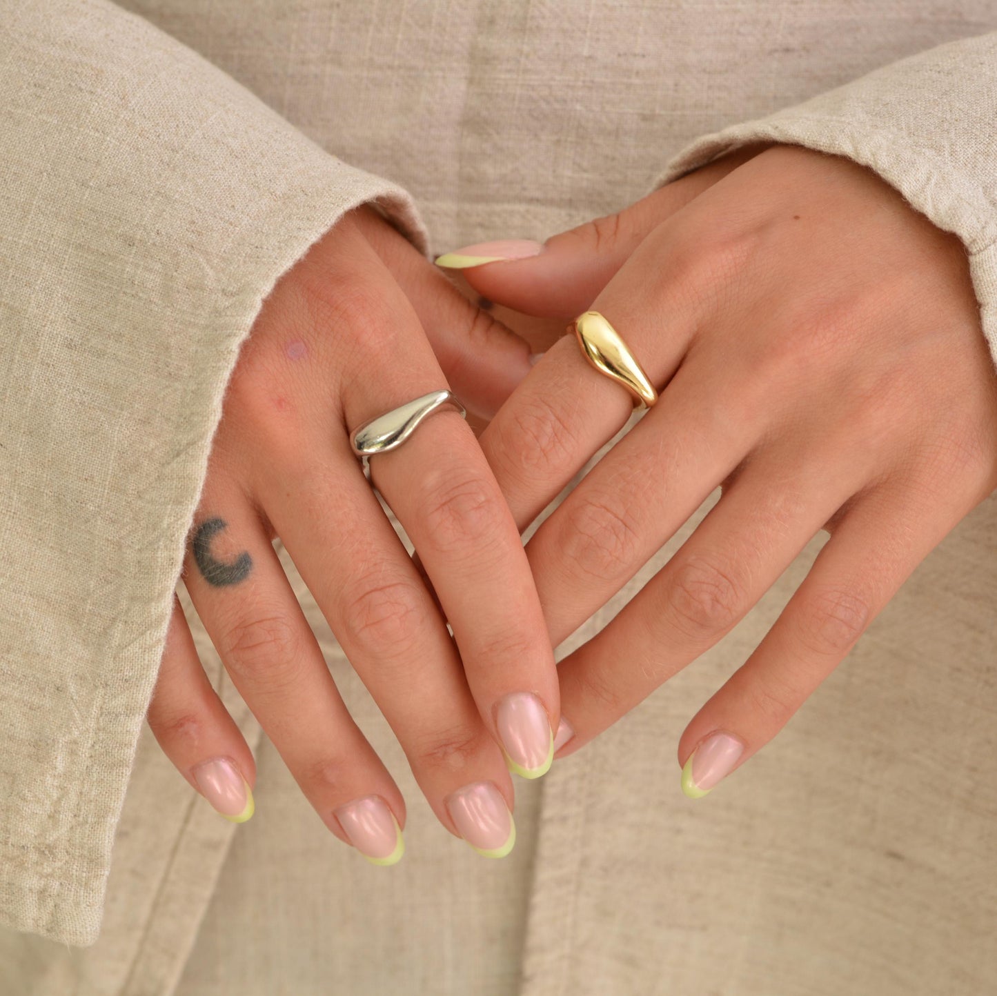 Close-up of hands with gold rings and light-colored nails against a neutral background