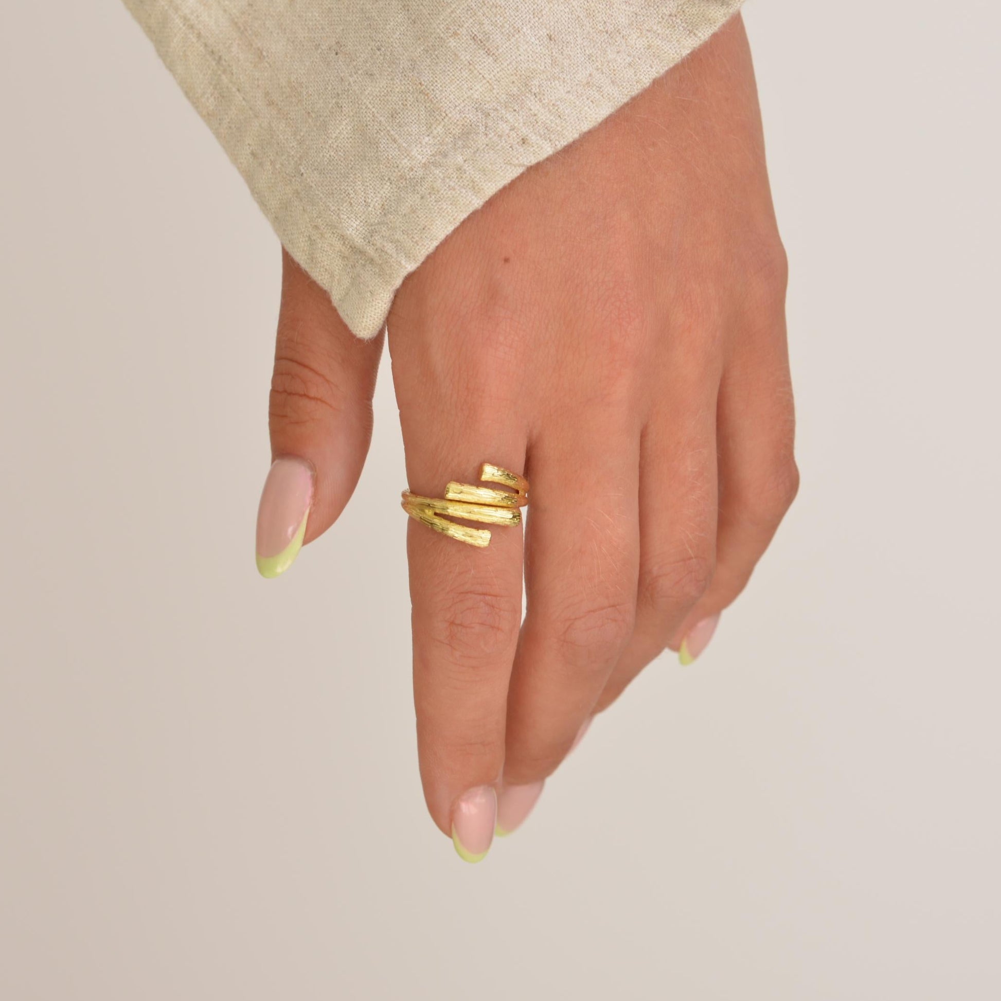 Hand wearing a gold ring on a neutral background