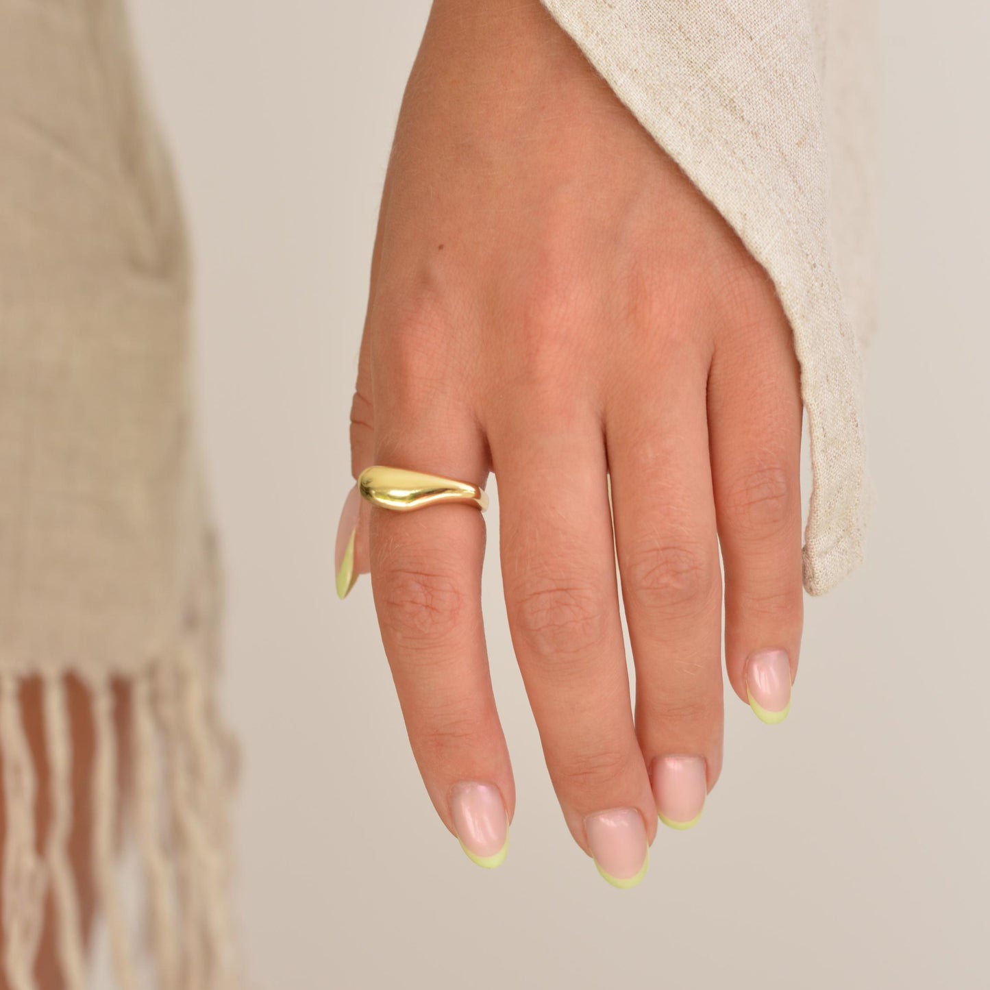 Hand wearing a gold ring with a neutral background