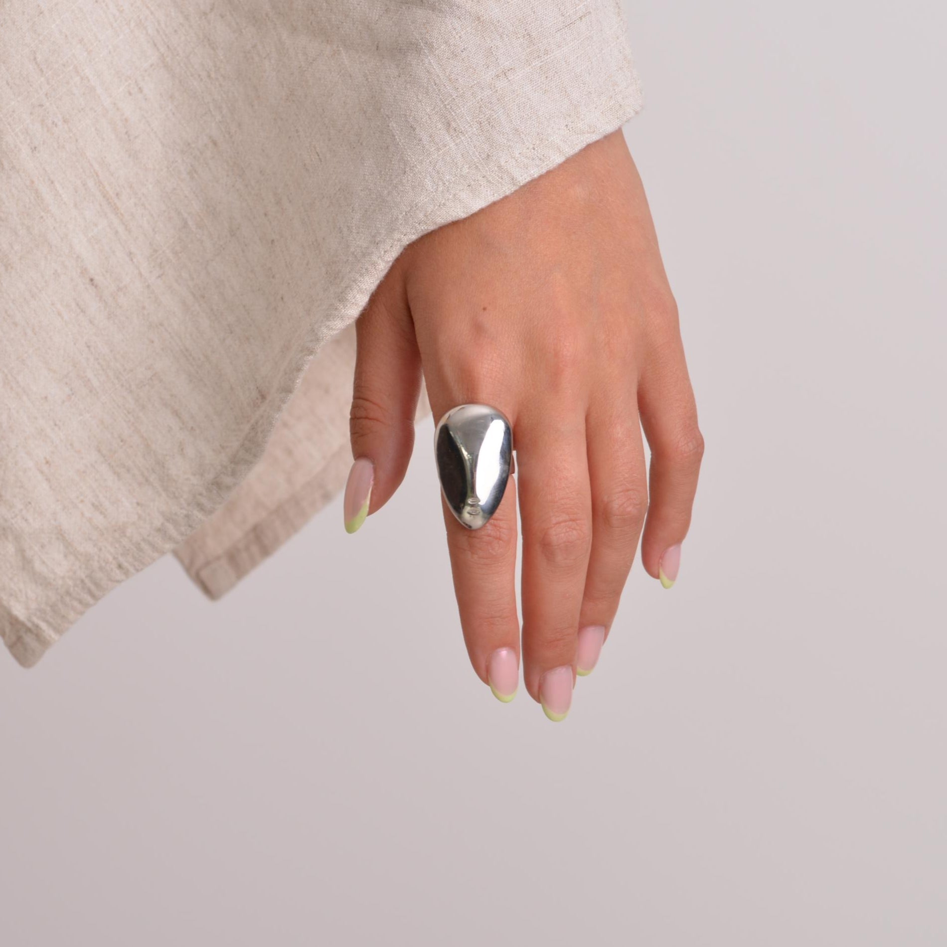 Close-up of a hand wearing a silver ring with a beige fabric background