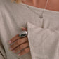Close-up of a person wearing a silver ring and necklace, with a neutral background.
