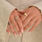 Close-up of hands with gold rings and light-colored nails against a neutral background