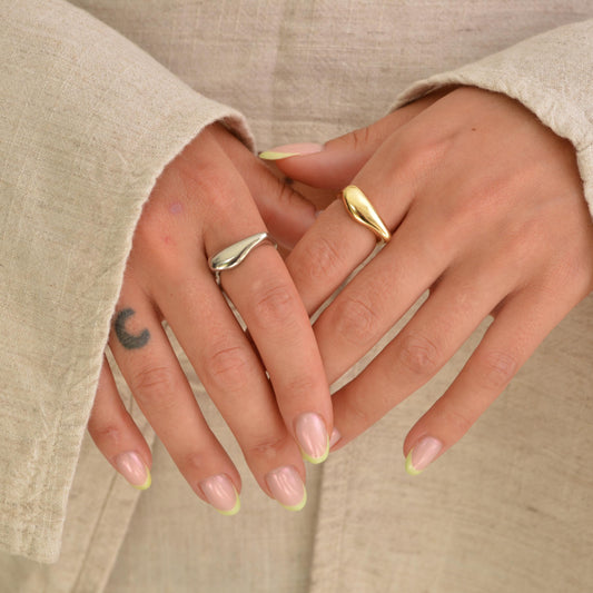 Close-up of hands with gold rings and light-colored nails against a neutral background