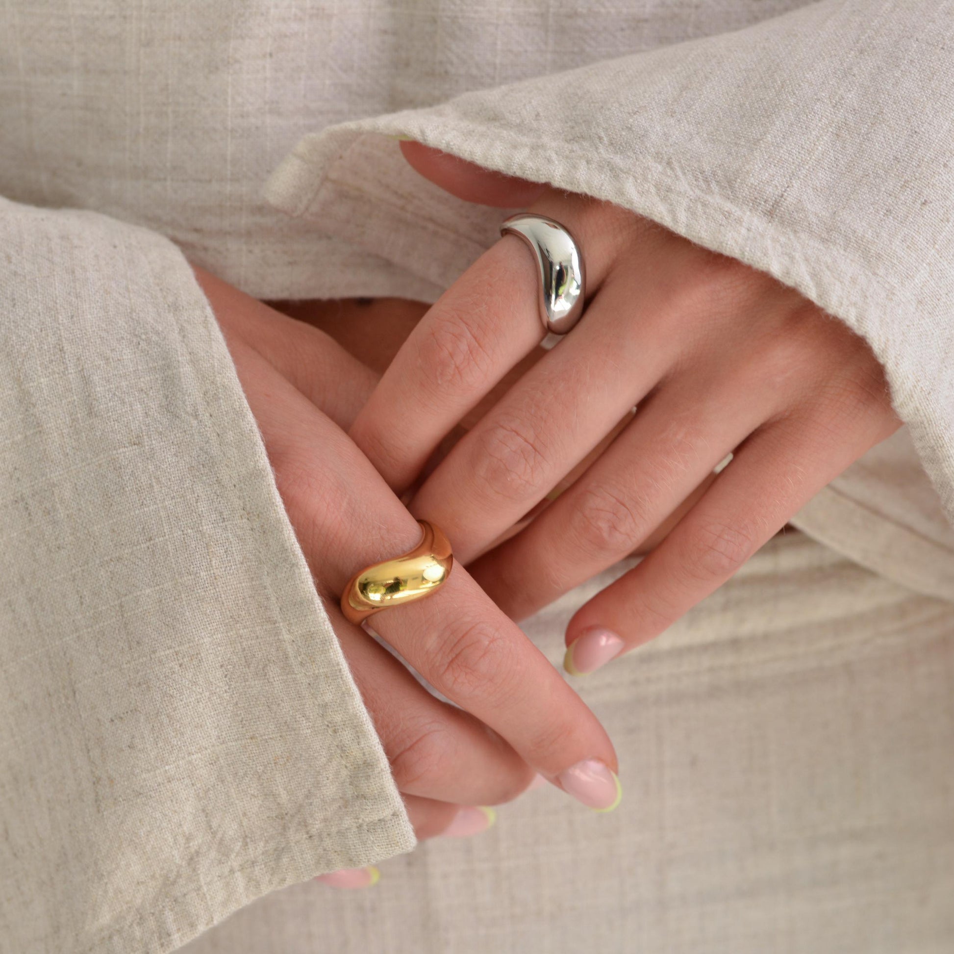 Close-up of hands wearing gold and silver rings with beige fabric background