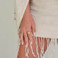 Close-up of a hand wearing a gold ring with a beige scarf draped over a shoulder.