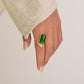 Hand wearing a gold ring with a green gemstone on a plain background