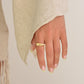 Hand wearing a gold ring with a plain background