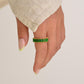 Hand wearing a green ring on a plain background