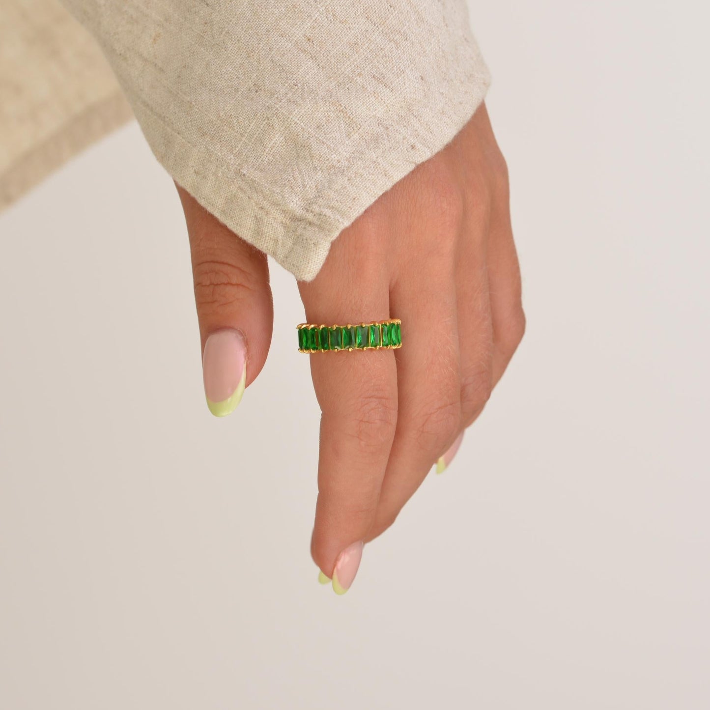Hand wearing a green ring on a plain background