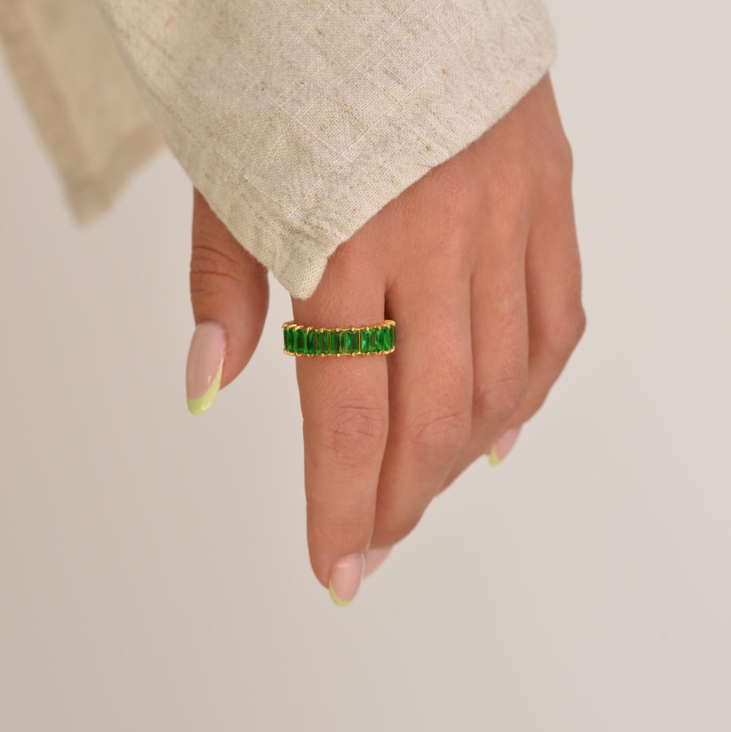 Hand wearing a green ring on a plain background