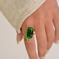Hand wearing a green ring with gold band on a neutral background