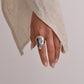 Hand wearing a silver ring with a beige sweater on a plain background