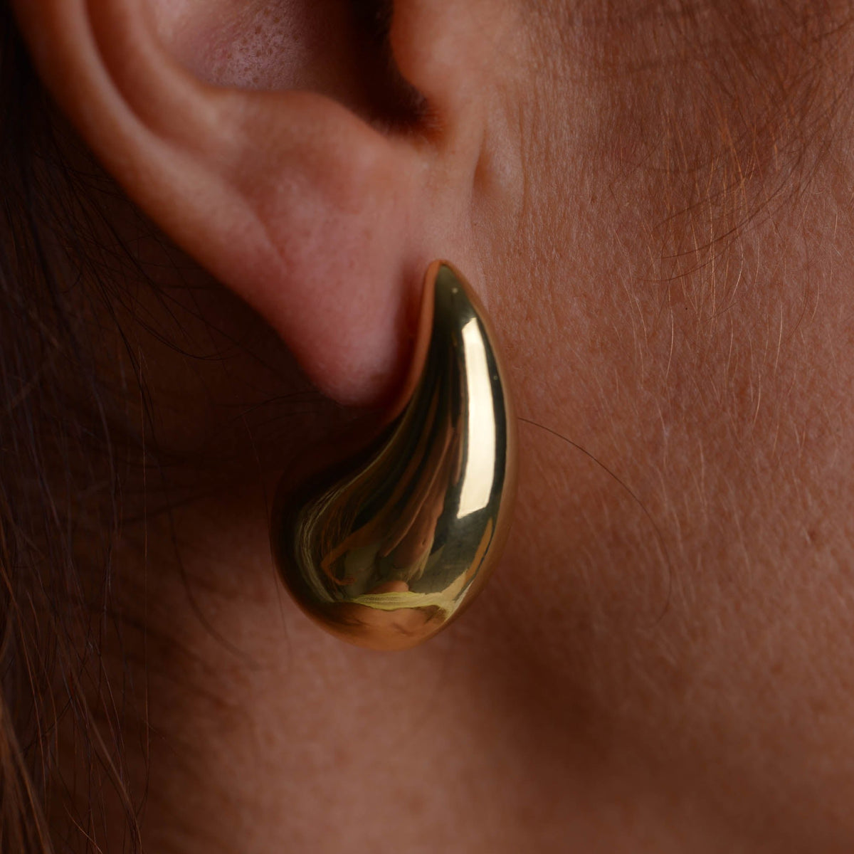Pair of chunky gold teardrop stud earrings with butterfly backs on a light grey background