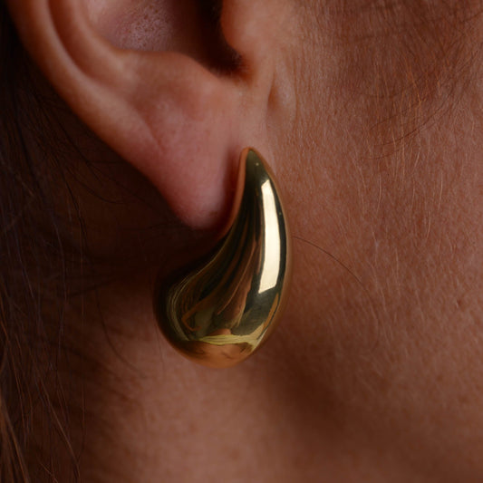 Pair of chunky gold teardrop stud earrings with butterfly backs on a light grey background