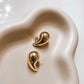 Pair of chunky gold teardrop stud earrings with butterfly backs on a light grey background