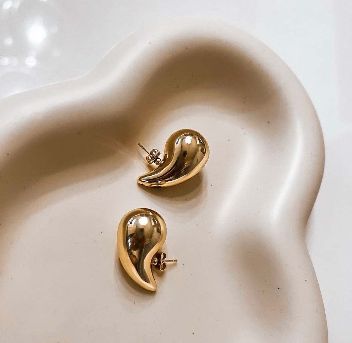 Pair of chunky gold teardrop stud earrings with butterfly backs on a light grey background