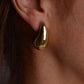 Pair of chunky gold teardrop stud earrings with butterfly backs on a light grey background