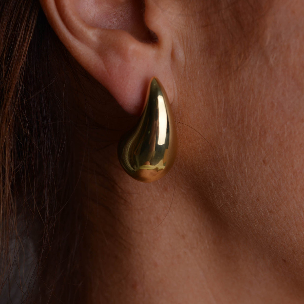 Pair of chunky gold teardrop stud earrings with butterfly backs on a light grey background