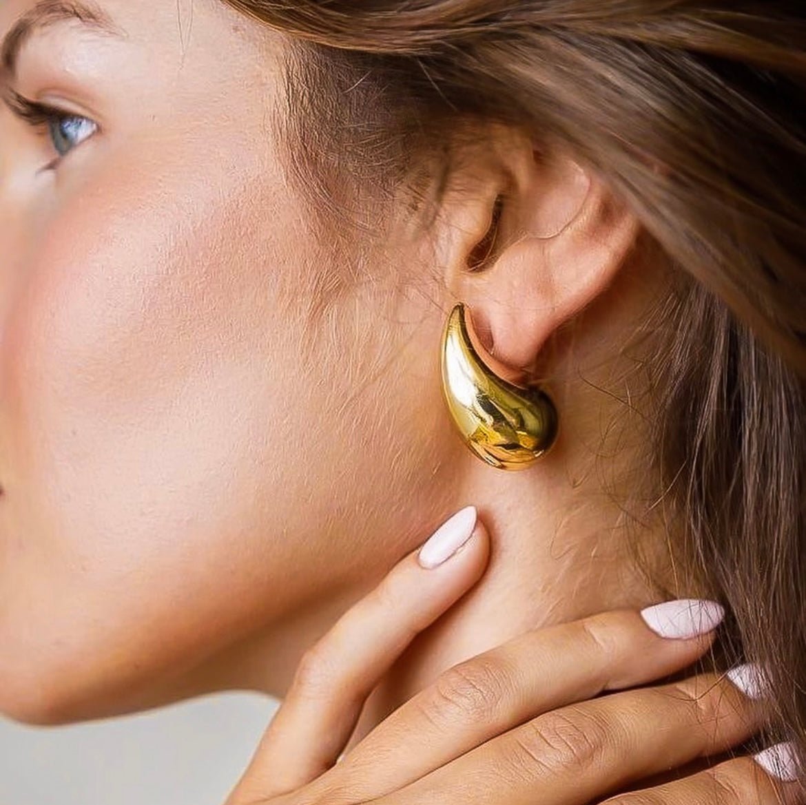 Pair of chunky gold teardrop stud earrings with butterfly backs on a light grey background