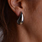Pair of chunky silver teardrop stud earrings with butterfly backs on a light grey background