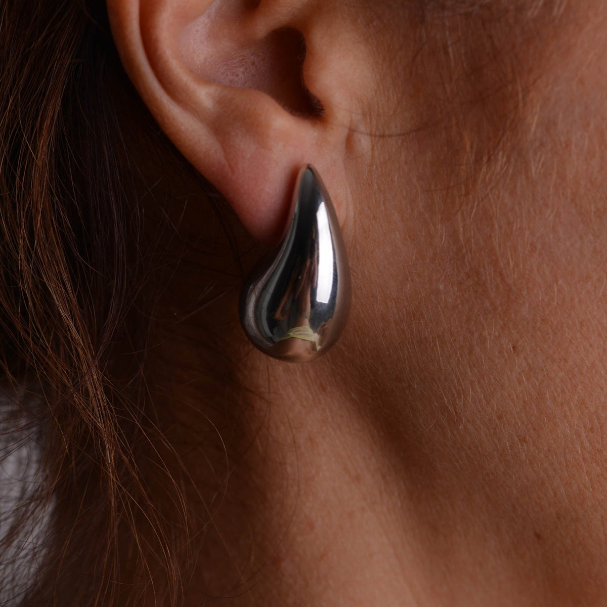 Pair of chunky silver teardrop stud earrings with butterfly backs on a light grey background
