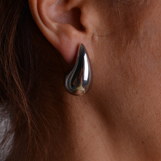 Pair of chunky silver teardrop stud earrings with butterfly backs on a light grey background