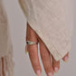 Hand wearing a silver ring with a beige sweater and blurred background